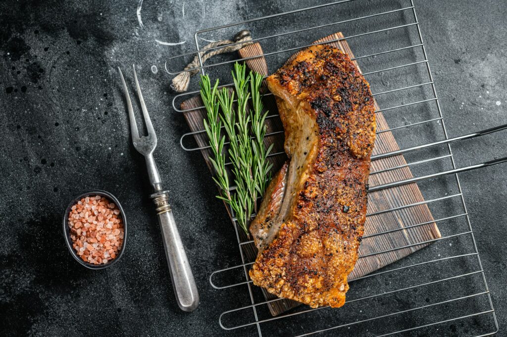 Grilled Pork belly meat on a grill with rosemary. Black background. Top view