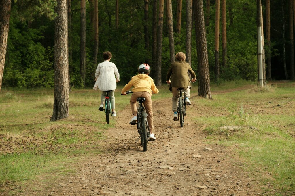 Rear view of active family of young parents and son cycling along forest path