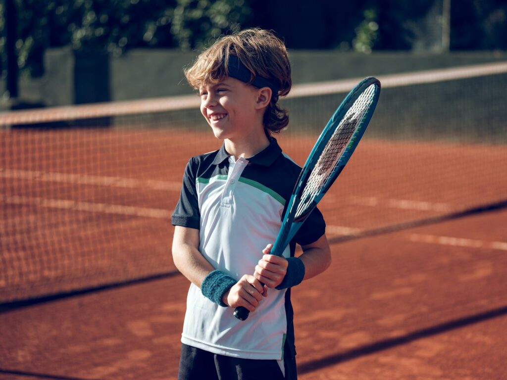 Cheerful adorable preteen boy in sportswear with tennis racket