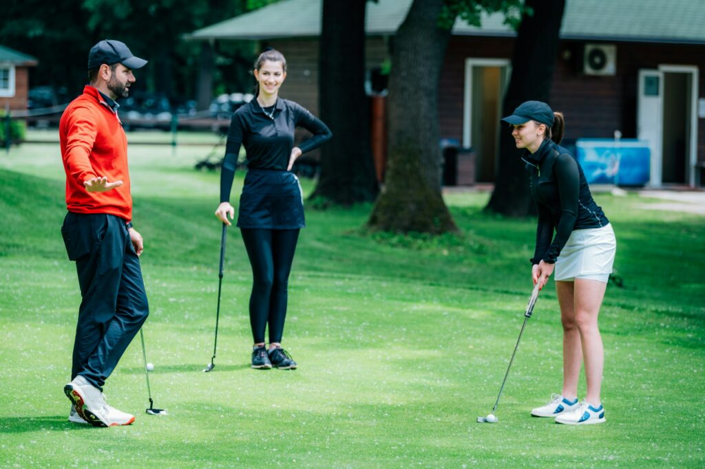 Golf putting lesson, two young female golfers practicing putting with golf instructor