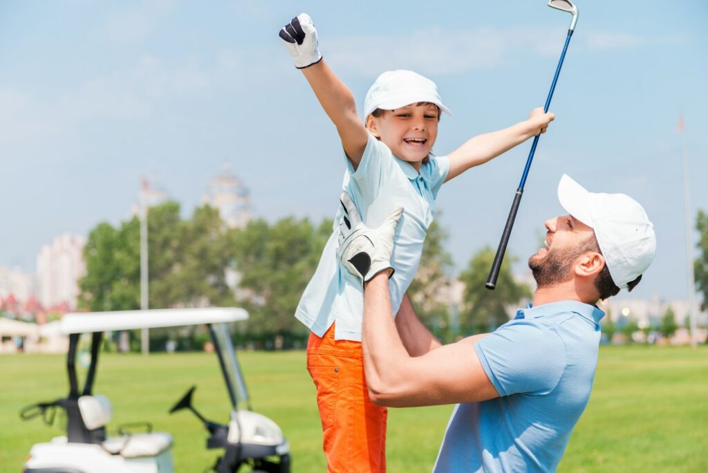 Joy of great game. Excited young man picking up his son while standing on the golf course