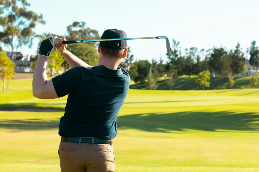 Rear view of caucasian young man playing golf with with golf club against clear sky at golf course