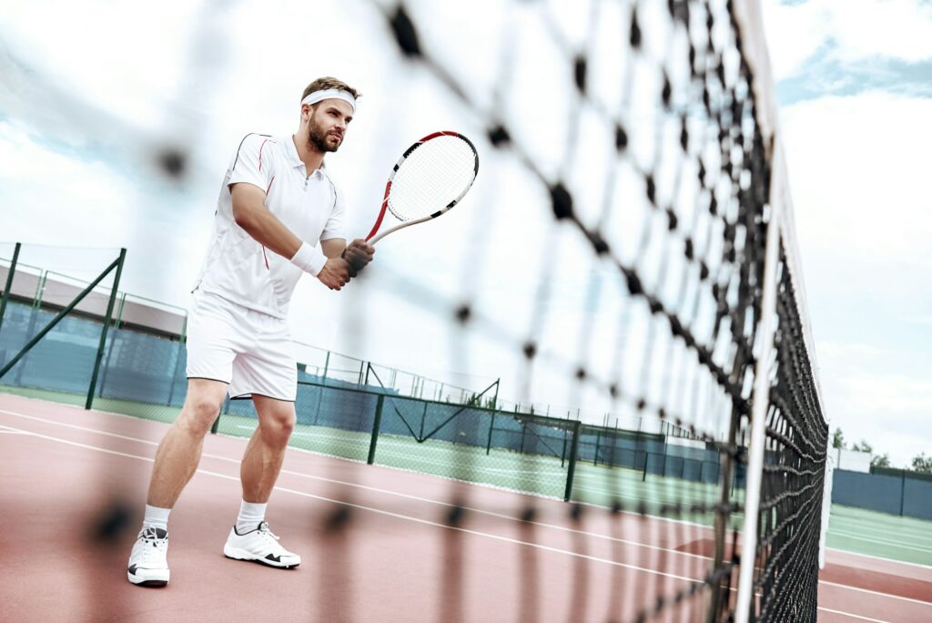 Tennis player is getting ready for the game. Handsome tennis player is standing on the court, near