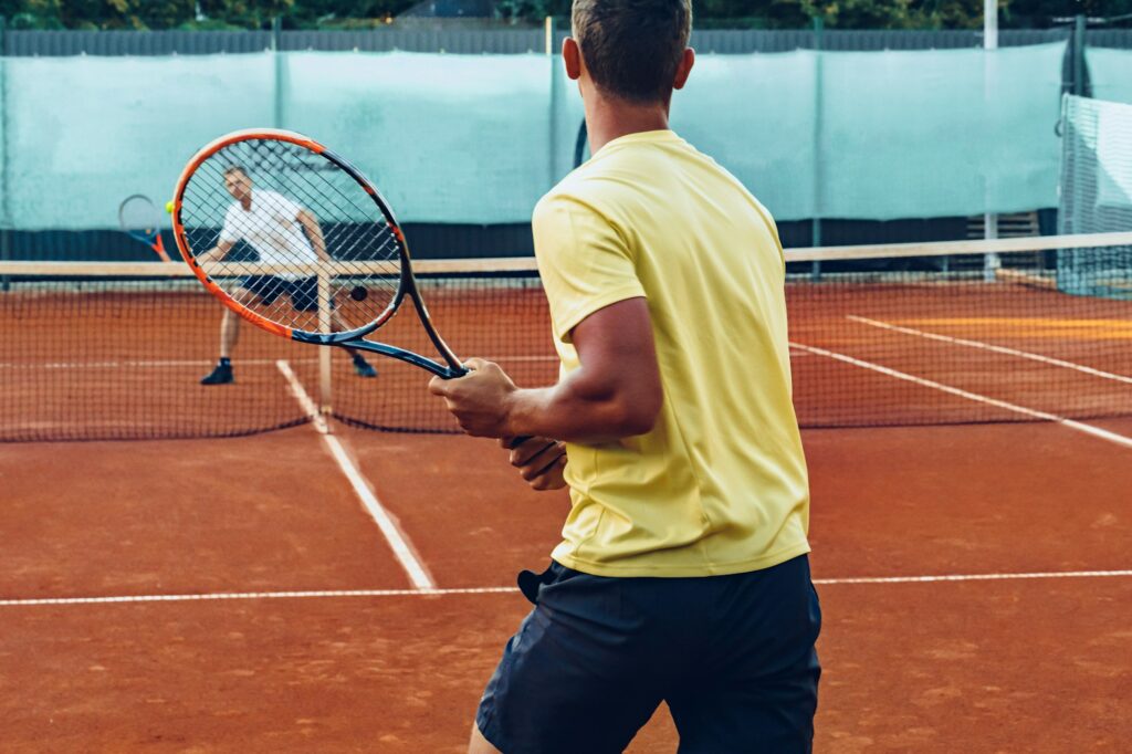 Two men playing tennis on clay tennis field