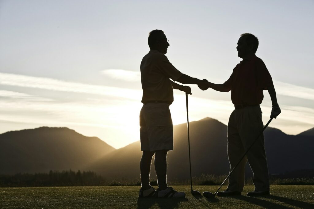 Two senior friends approach the first tee of a golf course at sunrise.