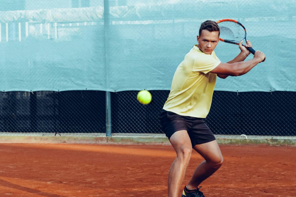 Young handsome man playing tennis on the tennis court